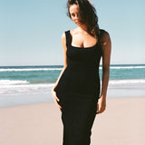 A woman on the beach wearing black textured bodycon midi dress with inbuilt bra support, square neckline, side split. 