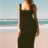 A woman on the beach wearing black textured bodycon midi dress with inbuilt bra support, square neckline, side split. 