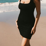 Close up at the beach  of black textured bodycon mini dress with inbuilt bra support, square neckline. 