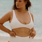 Woman in a white high waisted bikini standing on a beach with ocean in the background
